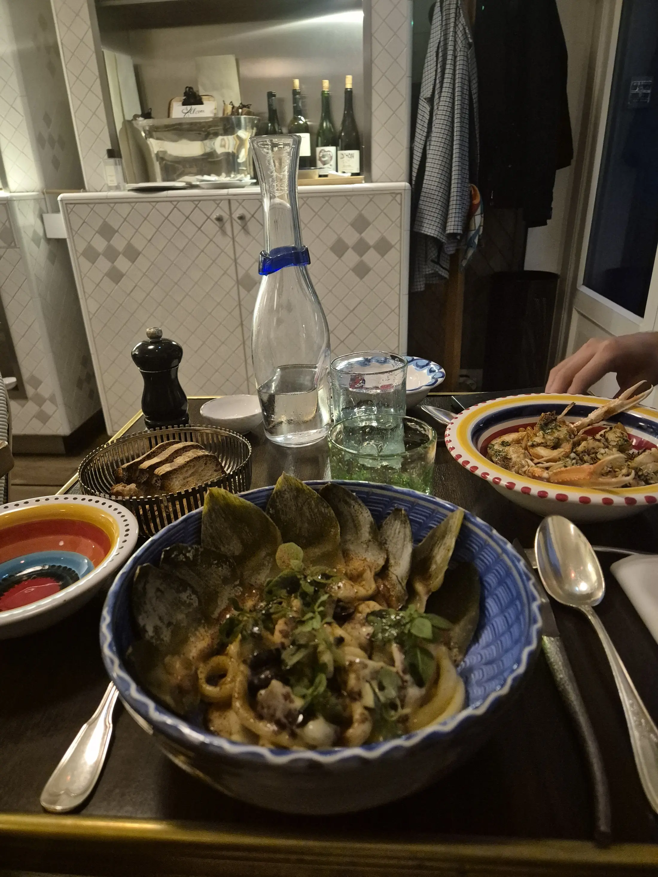 Two elegant bowls of seafood pasta on a cozy restaurant table, wine bottles behind.